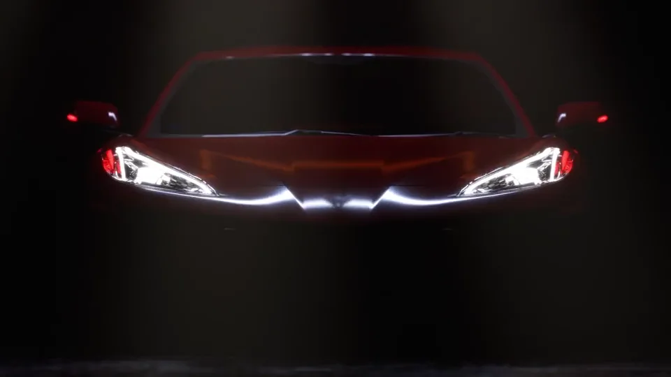 A sports car’s headlights and red body emerging from darkness